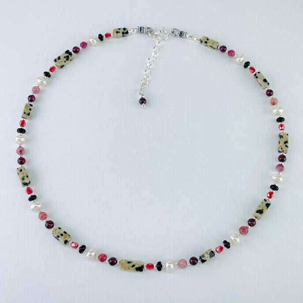 There is a pattern of beads that is repeated around the necklace. The pattern is:-  a rectangular cream with black spots ( like a dirty dalmation dog!), a tiny silver ball, a small  deep pink oval bead, a tiny silver ball, a small flat round bead, a tiny silver ball, a larger white pearl, a tiny silver ball, a round opaque pink bead, a tiny silver ball, a small deep red round bead and a tiny silver ball. This is repeated 10 times. It ends with a shiny silver link chain and a little red bead. 