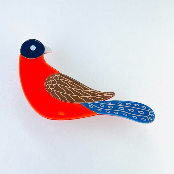 A brightly coloured bird made up of four blocks of colour. The head is dark blue, with a paler eye and beak, turned to face backwards. Then a bright red body with a brown and cream patterned wing attached to the right. Just below this a bright blue tail stretches out horizontally.