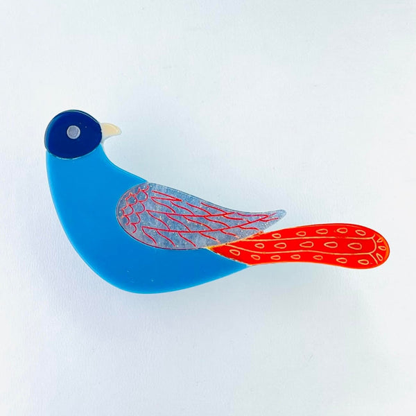 A brightly coloured bird made up of four blocks of colour. The head is dark blue, with a paler eye and beak, turned to face backwards. tTen a bright blue body with a blue and orange patterned wing attached to the right. Just below this a bright orange tail stretches out horizontally.