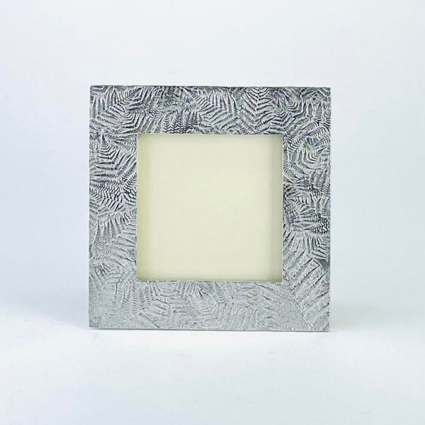 A square pewter photo frame with a fern leaf design arranged around the frame in a random form