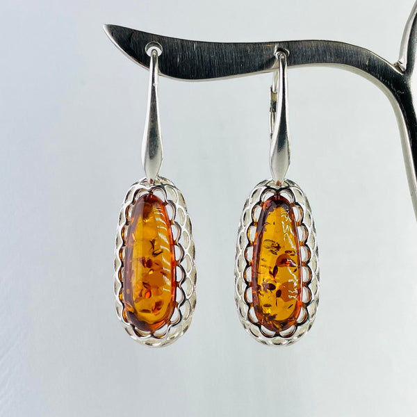 pear shaped orange amber stone, with lots of little fossilised seeds pods, are surrounded by a double layer of silver scallop shapes. Attached to a solid fronted silver hook.