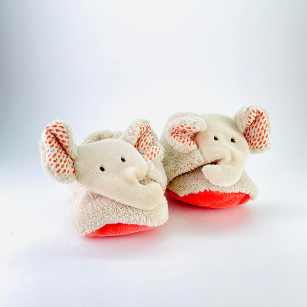 Pale beige bootie type slippers with an elephant face on the front. There is long trunk, two little eyes and big ears with an orange fish design on the inside,  The soles of the slippers a                                                             