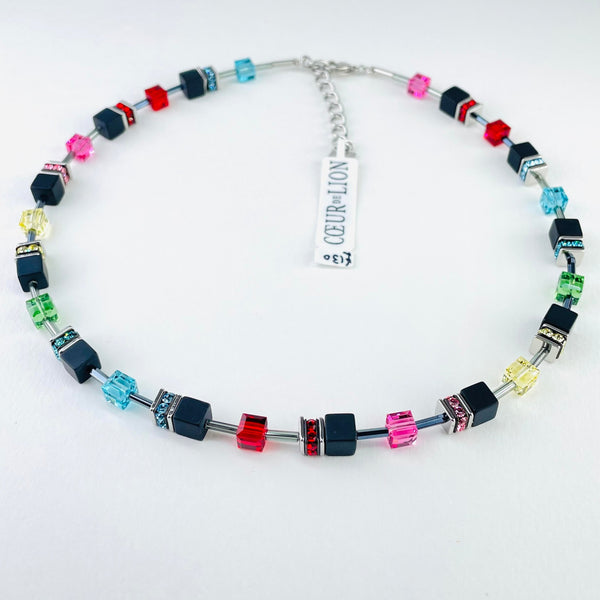 Beaded necklace with modern square beads displayed around it.. The colours are black, red, pink, yellow, blue, green. The beads are in a pattern around the necklace - two beads, then silver rondelles,  one bead then silver rondelles, then repeated. Each set of double beads has one black one, each single bead is brightly coloured. 