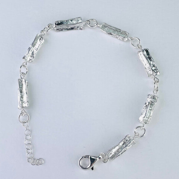 A bracelet made up of seven rectangular links . They are all textured silver, a texture that looks a little like the bark of the tree.  They are linked by round jump rings and finished with a heavy lobster catch. A plain silver chain hangs at the end of the bracelet with a little silver bead at the end ( so it can be worn a little longer)
