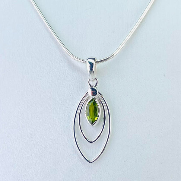 A marquise shaped faceted peridot stone hangs inside, and to the top of , two separate marquise silver outlines, one smaller than the other. All connected at the top by a silver circle on a silver bail.