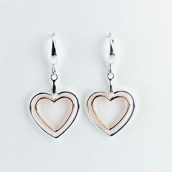 Two heart outlines, one inside the other. The outer one is polished silver, the inner one is rose gold plated. They are attached at the top by a silver rod which is attached to a high polished hook by a silver ring.
