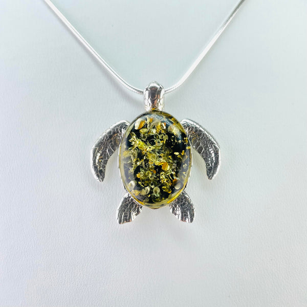 Cute turtle pendant. The body is formed of a mossy green amber with lots of little inclusions, surrounded in a silver mount. Everything else is made from silver.The chain is slipped through the head, as if he is holding it in his mouth. The flippers, well engraved to look like turtle skin are at either side of the body, as if we are looking at the turtle from above as he swims through the sea.