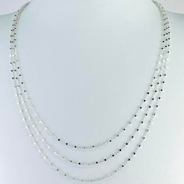 One necklace made of three strands, that sit at different lengths equally spaced around the neck, getting a little longer at the front. Each chain is basically formed of small circular links with a silver cube, about the same width, after every 5th round link.