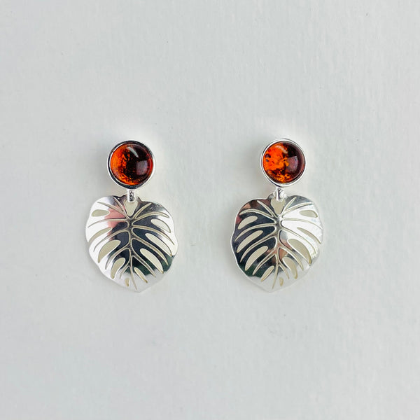Round pieces of green amber are set into silver with a silver  skeleton leaf shape hanging below . The leaf looks like a palm leaf, the amber is a sage green colour.