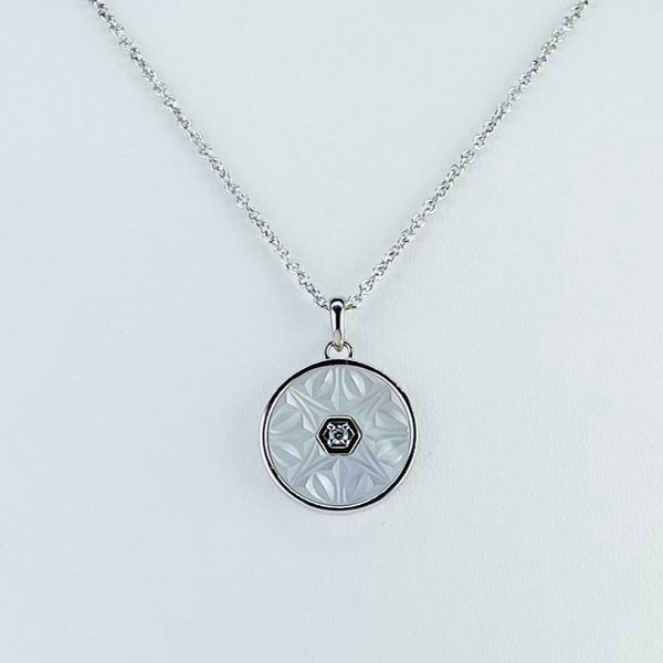 A round pendant, mostly formed of  creamy mother of pearl framed in silver. The mother of  pearl has been delicately carved with triangle and bean shapes. In the centre, within a small silver hexagon, is a shiny cubic zirconia stone. All hanging from a silver chain by a simple bail.       