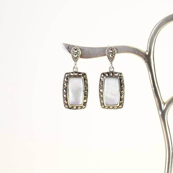 an obling white mother of pearl stone is framed in little sparkly marcasite stones hanging off a stud fitting.