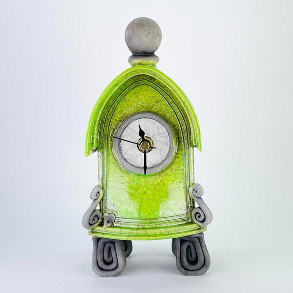 This quirky clock has the shape of a gothic arch or the porch of an old church, with a little roof effect on the top. It has four feet formed of square spirals of matte dark grey, a scroll at each side of the front with a tiny mouse head peering out! It is topped with a matte grey orb. The main body is a bright lime green colour, the central round face is white and it has a minute, an hour and a second hand - all black.