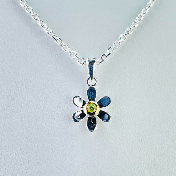 A small flower pendant with six evenly spaced high polished rounded petals. In the centre is a round lime green peridot stone surrounded by gold plated silver.  It hangs off a silver bail, connected by a small silver ring . The pendant hangs off a silver link chain .      
