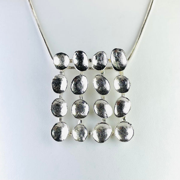 Silver necklace with a large grid design at the front. The grid is formed of 16 coffee bean shaped nuggets in four rows of four .