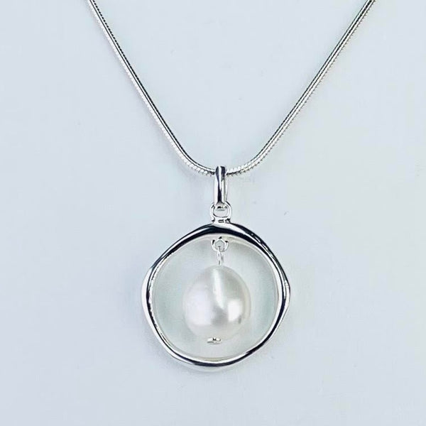 A high sheen slightly off oval pearl is suspended in a round silver outline. The silver is a 'wobbly' circle, slightly thicker in some parts than others. The pearl hangs loosely - so it can move. All attached to a plain silver bail and on a snake chain.