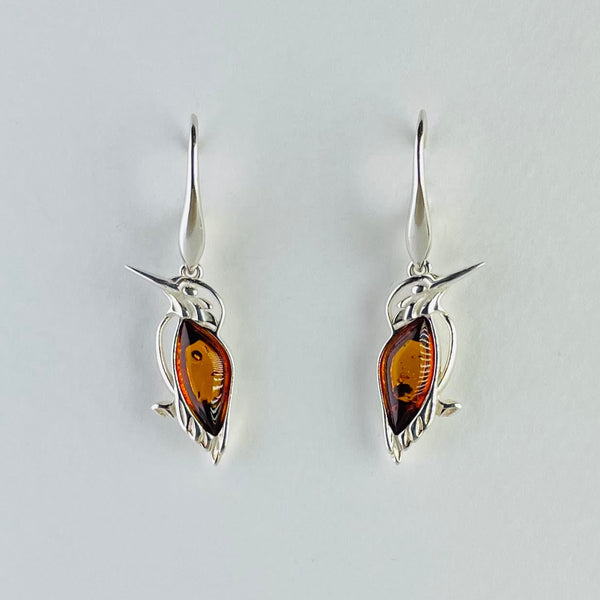 Each earring is a kingfisher facing to the side ( mirror image) attached to an elegant solid silver hook, slightly wider at the bottom. The kigfisher has a golden amber wing. smooth and mostly clear. The tummy is formed of a silver strand as are the tips of the wings. They have long slender pointed silver beaks, eyes and a little foot at the bottom.