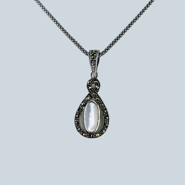 The pendant is a tear drop shape with an additional little twist at the top.The outline is set with round sparkly marcasite stones. Set in the centre of the tear drop is a long oval piece of mother of pearl, framed in silver. The whole thing hangs off a silver bail set with marcasite and it hangs on an oxidized dark silver chain.