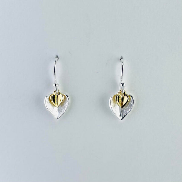 Earrings made of two separate hearts. A much smaller gold plated one sits on top of, and at the top of, a larger satin silver one. They are slightly  concave in shape on a silver hook.