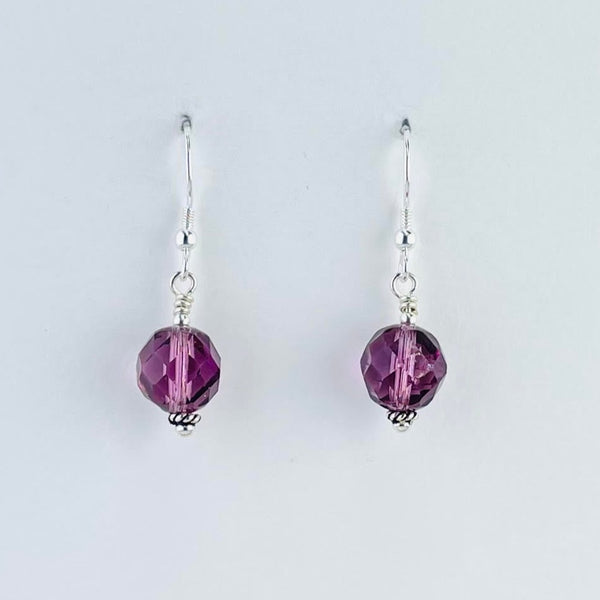 Pretty lilac purple faceted glass bead earrings, with a tiny little silver bead at the bottom, are connected to a silver hook by a small silver circle.