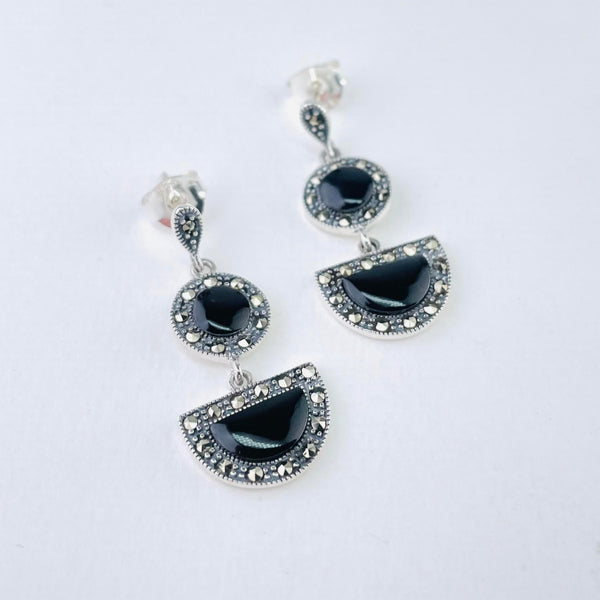 The earrings are formed of three parts. At the top is a small upside down tear drop, set with little sparkly marcasite stones. Below that is a larger circle with a shiny black onyx stone in the centre surronded by sparkly marcasite stones. Below that is a larger semi circle, sitting horizontally, again set with an onyx and marcasite stones. Each shape is attached to the other by small silver rings.